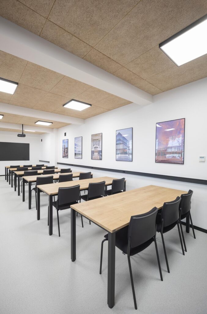 Pusta nowoczesna sala lekcyjna z rzędami drewnianych stołów, czarnych krzeseł, projektorem i tablicą na ścianie