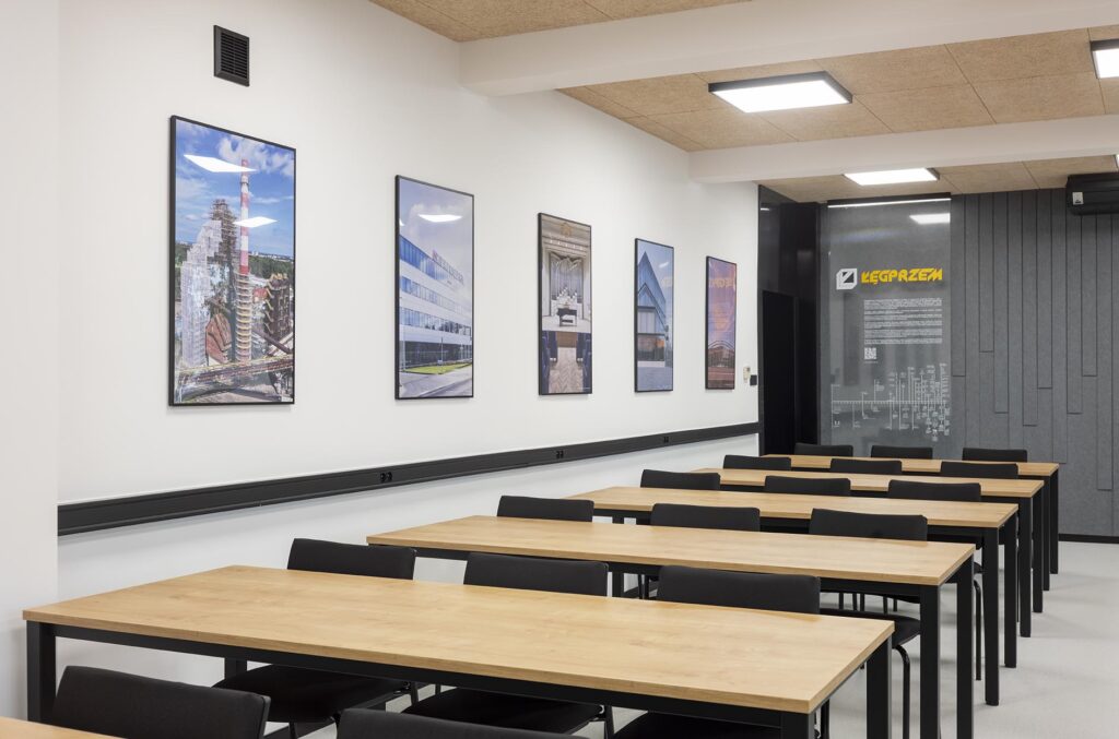 Pusta nowoczesna sala szkoleniowa z drewnianymi stołami, czarnymi krzesłami i obrazami na białej ścianie