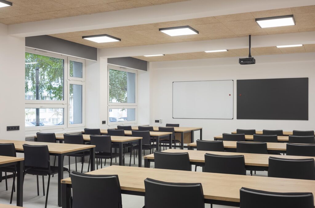 Pusta nowoczesna sala lekcyjna z rzędami biurek i krzeseł, tablicami na ścianie i projektorem