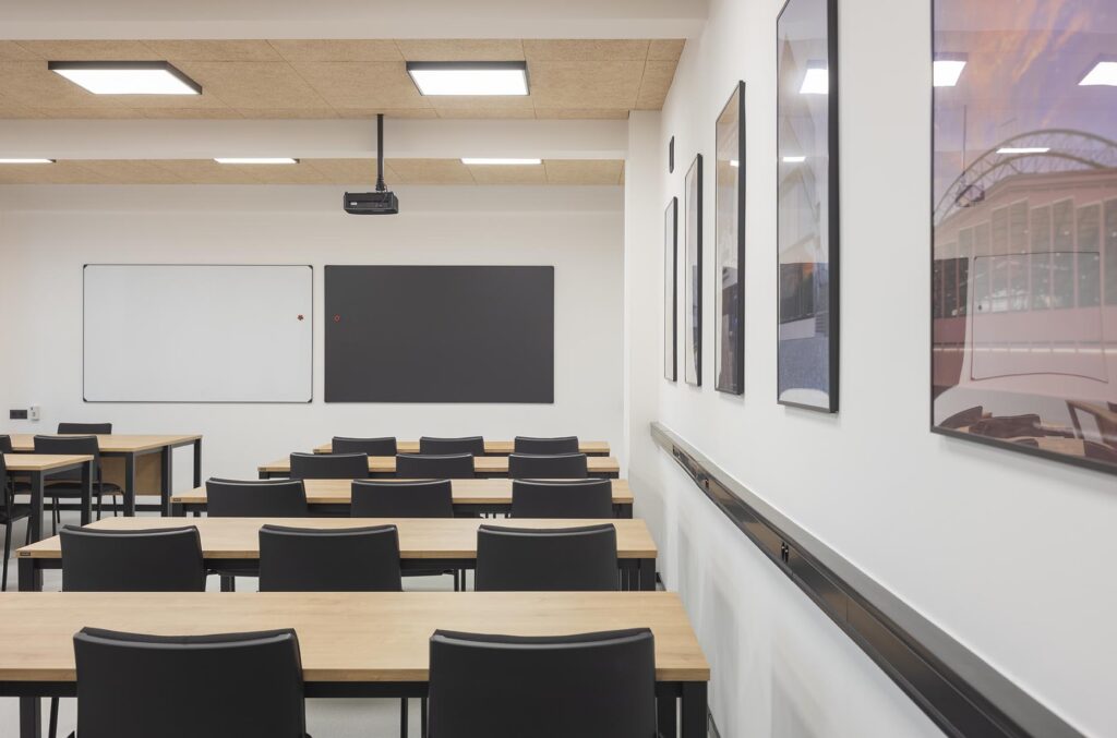Pusta nowoczesna sala lekcyjna z rzędami drewnianych stołów, czarnymi krzesłami, tablicami i projektorem