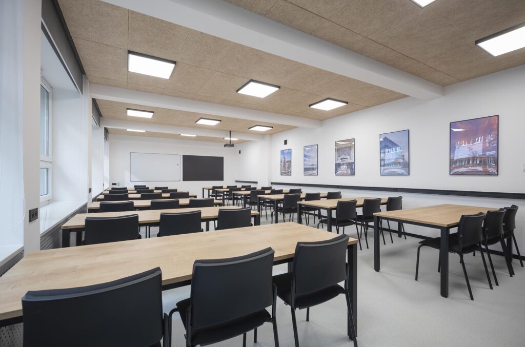 Pusta nowoczesna sala lekcyjna z rzędami stołów i krzeseł, tablicą i obrazami na ścianie