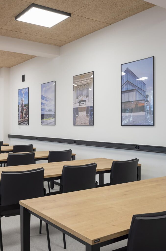 Nowoczesna sala szkoleniowa z drewnianymi stołami, czarnymi krzesłami i obrazami na białej ścianie