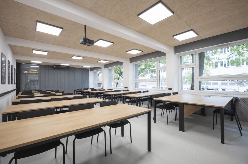 Pusta nowoczesna sala lekcyjna z drewnianymi stołami, czarnymi krzesłami, projektorem i dużymi oknami