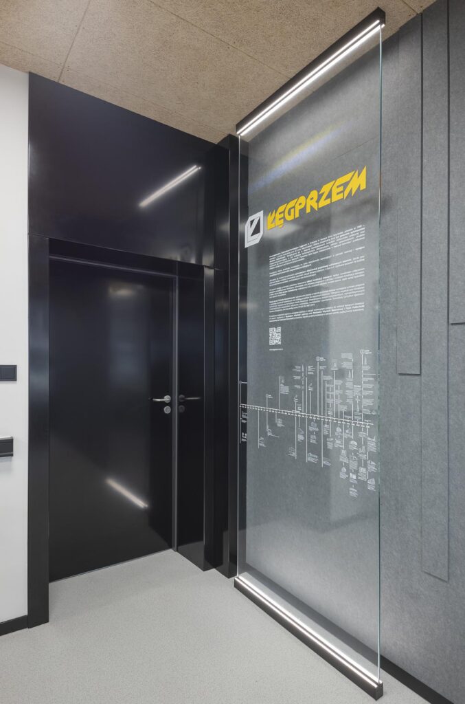 Nowoczesne wnętrze biura z czarnymi drzwiami i podświetloną szklaną tablicą informacyjną z żółtym logo