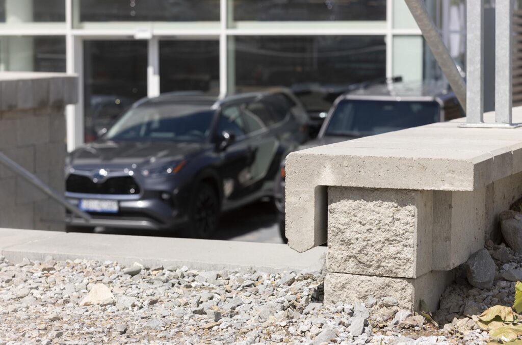 Betonowe bloczki i żwir na placu budowy, w tle rozmyte zaparkowane samochody przy szklanej fasadzie