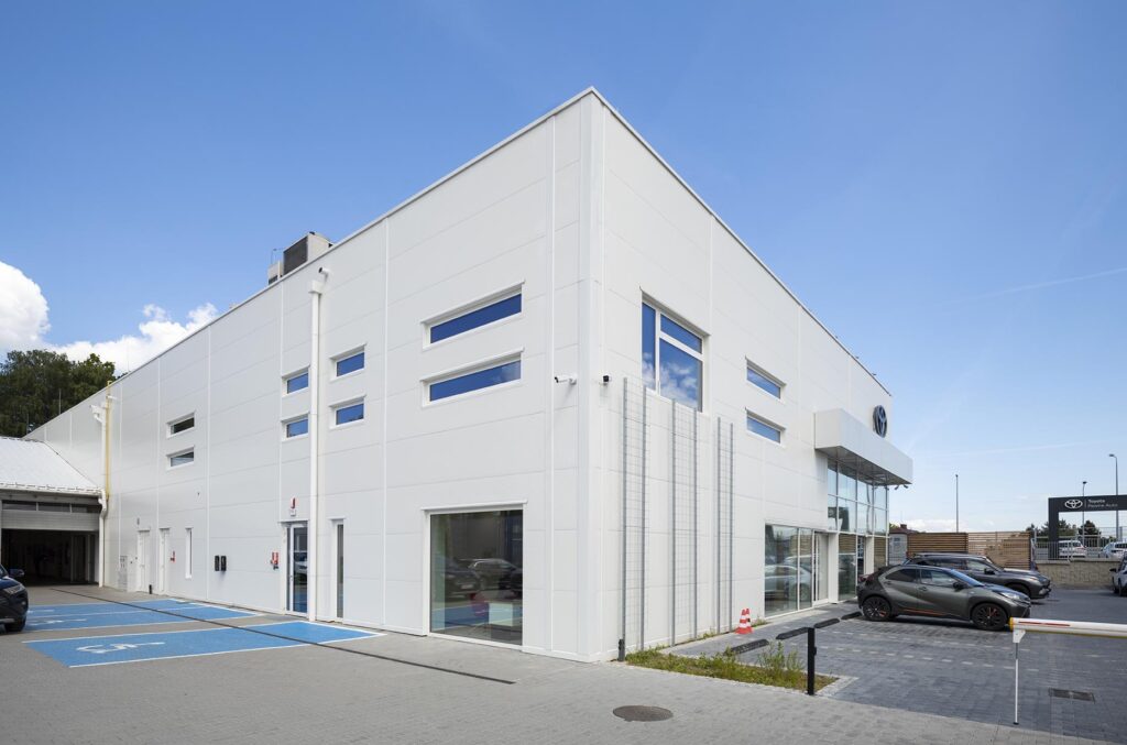 Nowoczesny biały budynek komercyjny z parkingiem i wydzielonymi miejscami dla niepełnosprawnych
