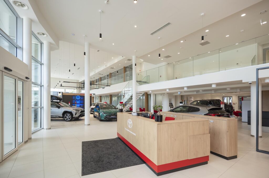 Jasny, nowoczesny salon samochodowy Toyota z drewnianą recepcją i kilkoma wystawionymi autami