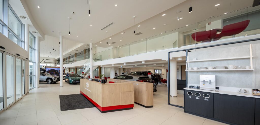 Przestronne, nowoczesne wnętrze salonu samochodowego z recepcją, wystawionymi autami i przeszkloną antresolą
