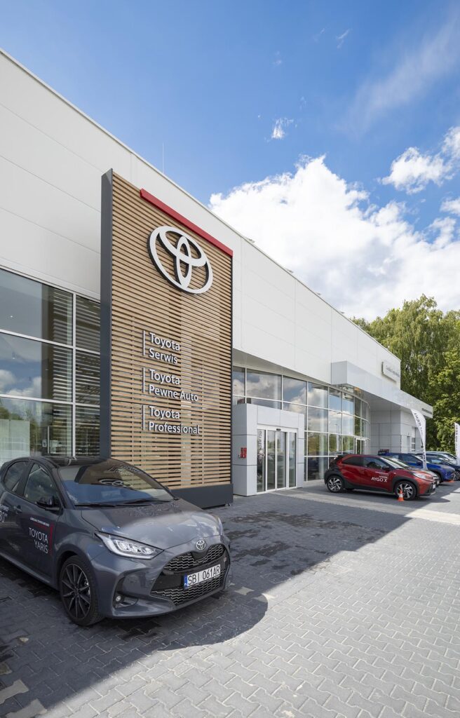 Salon Toyoty z dużym logo, na pierwszym planie szara Toyota Yaris
