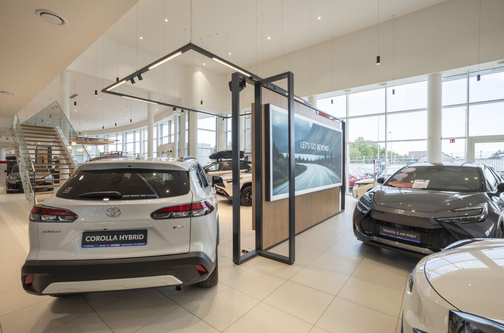 Wnętrze salonu samochodowego z widoczną srebrną Toyotą Corolla Hybrid i innymi autami