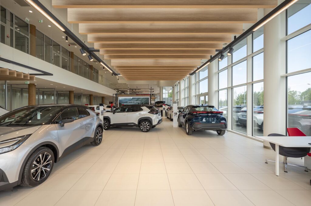 Wnętrze nowoczesnego salonu samochodowego z kilkoma wystawionymi autami, dużymi oknami i drewnianymi belkami sufitowymi