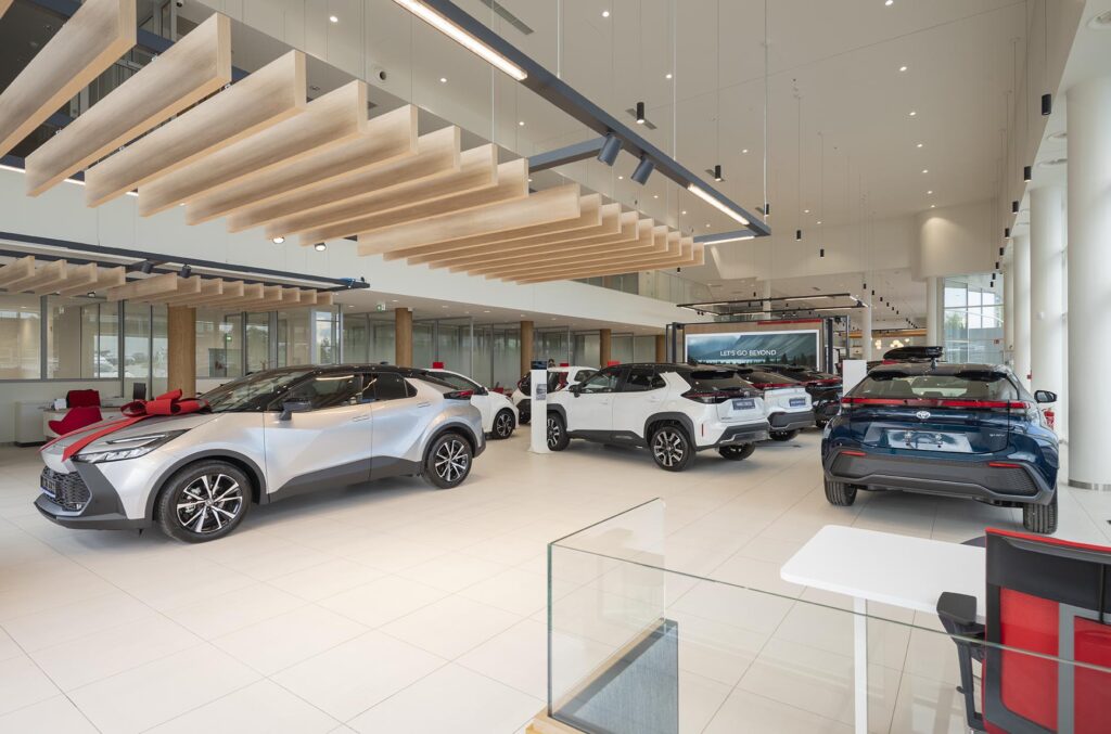 Nowoczesny, jasny salon samochodowy z wystawionymi nowymi autami i drewnianymi panelami sufitowymi