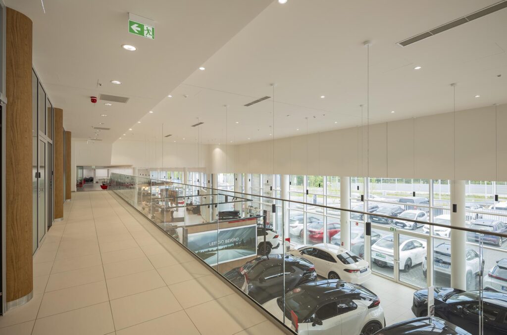 Wnętrze nowoczesnego salonu samochodowego z antresolą i przeszkloną balustradą, widok na wystawione samochody