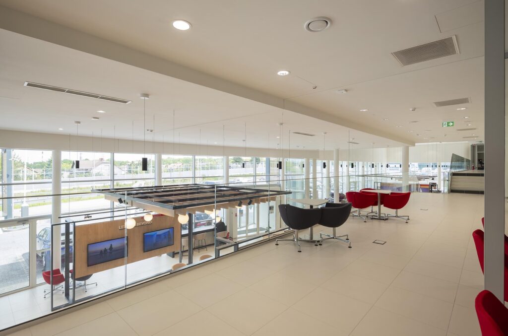 Przestronne, jasne wnętrze salonu wystawowego z antresolą, czerwonymi i czarnymi fotelami oraz dużymi oknami