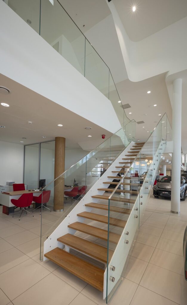 Nowoczesne wnętrze z drewnianymi schodami i szklaną balustradą w salonie samochodowym