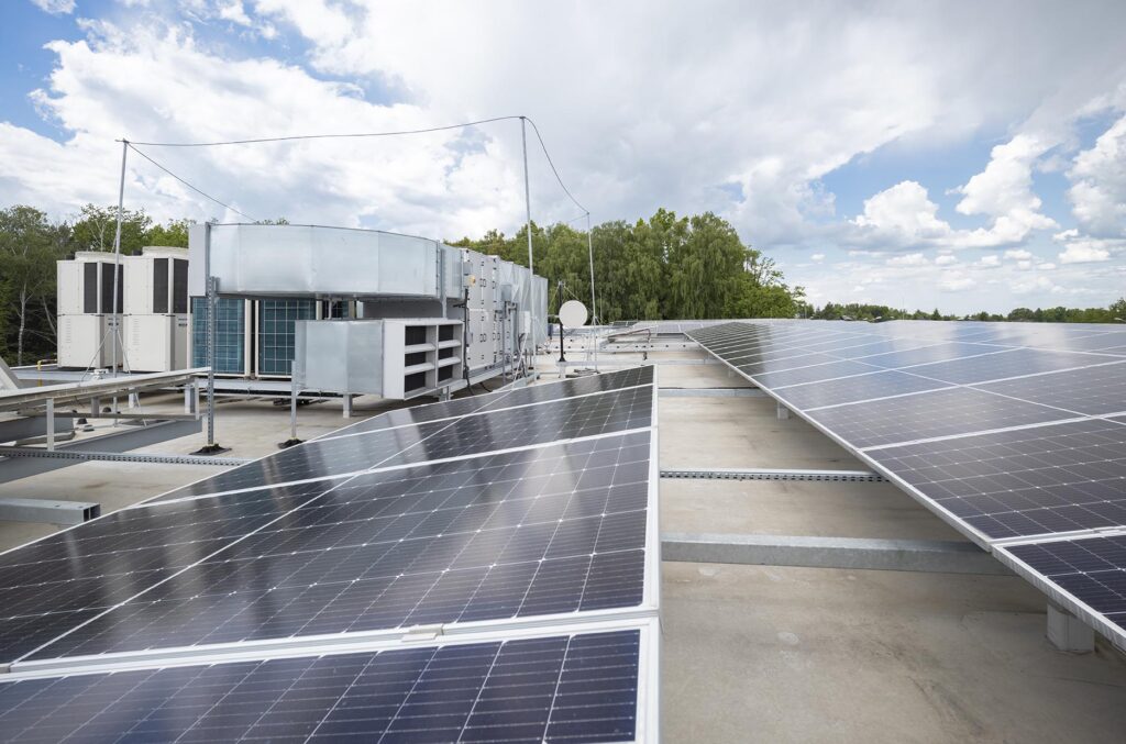 Panele fotowoltaiczne na płaskim dachu z urządzeniami HVAC i drzewami w tle